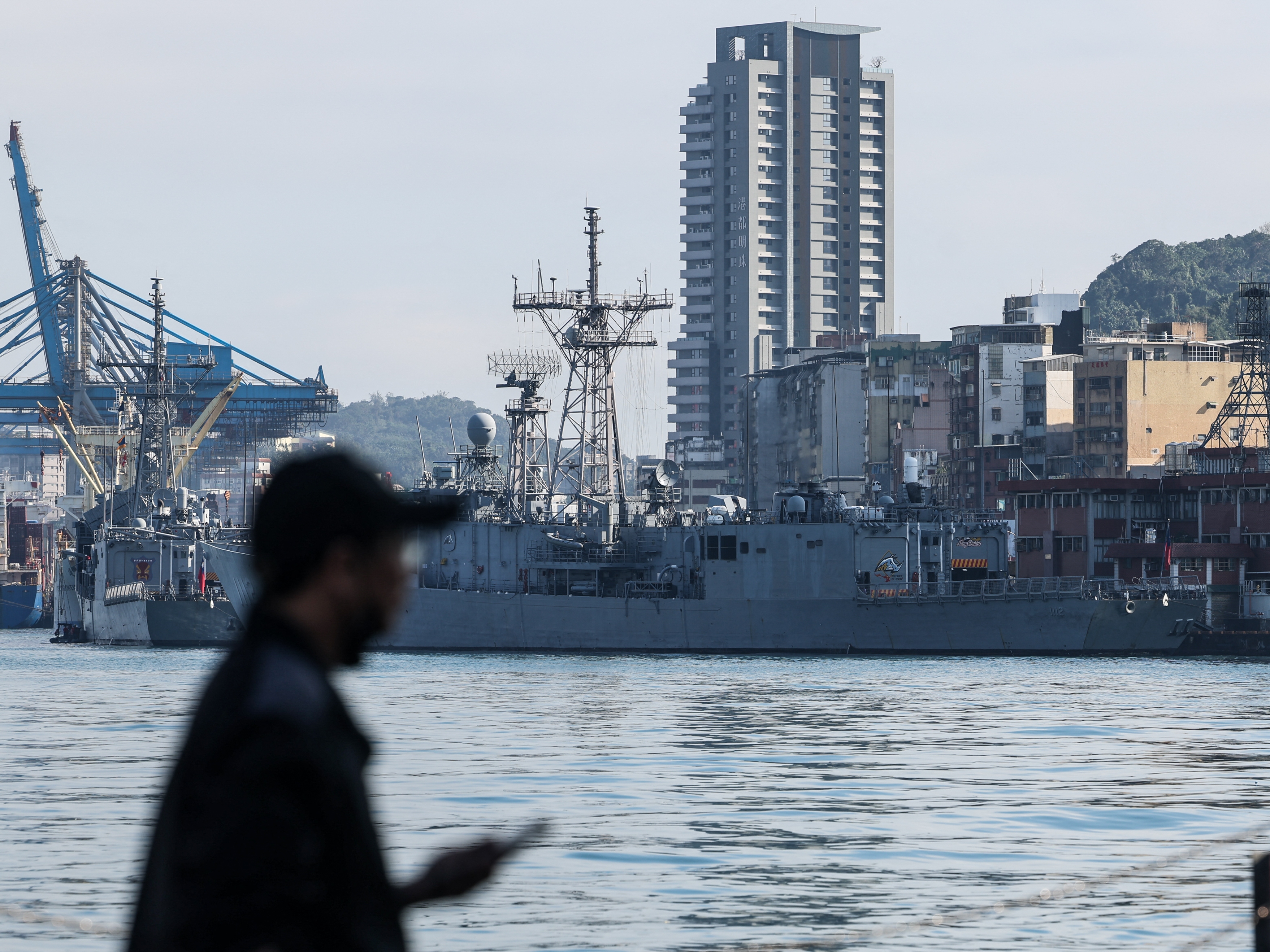 caption: A man stands in front of Taiwanese navy ships anchored at the harbor in Keelung, near Taipei in northern Taiwan, on Dec. 11, 2024.