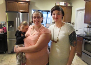 caption: U.S. Army Capt. Jennifer Peace (right) and her wife, Debbie, with their youngest daughter at their home in Spanaway, Wash.