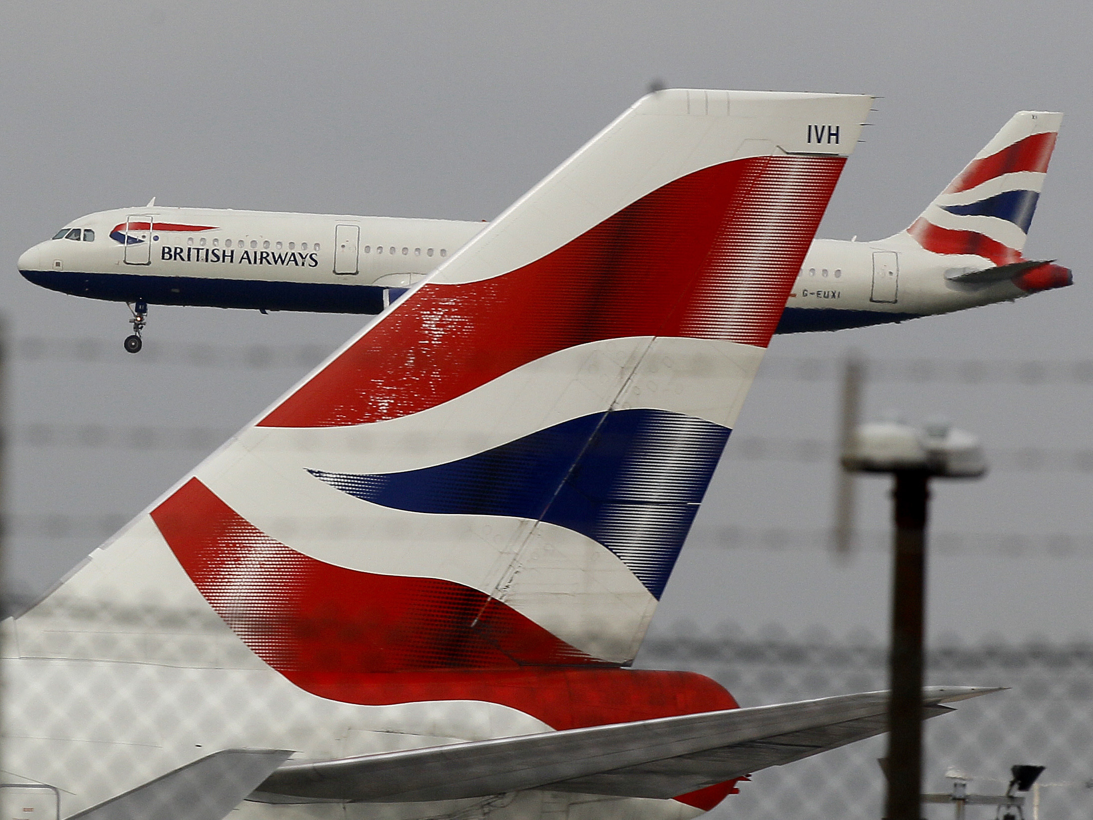 caption: A British Airways plane comes in to land behind a tail fin at Heathrow Airport in London. On Friday, the head of the group that owns BA called for instituting an electronic health pass for passengers as the company announced steep losses due to COVID-19.