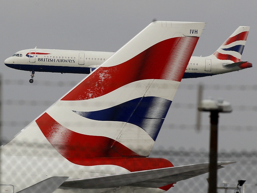 caption: A British Airways plane comes in to land behind a tail fin at Heathrow Airport in London. On Friday, the head of the group that owns BA called for instituting an electronic health pass for passengers as the company announced steep losses due to COVID-19.
