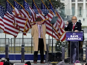 caption: John Eastman, attorney for former President Donald Trump, stands at left as Rudy Giuliani speaks in Washington at a rally in support of Trump.