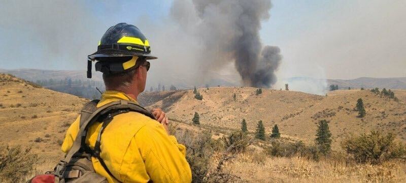 caption: A firefighter looks toward a blaze near Black Canyon, northwest of Yakima. 