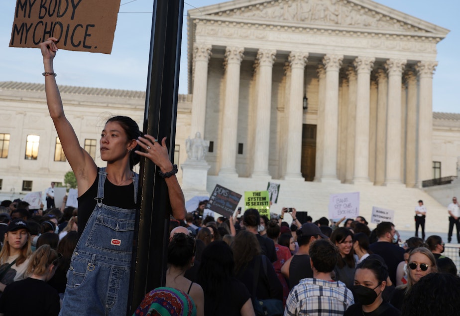 caption: A person holds a sign during a rally in front of the Supreme Court on Tuesday in response to its leaked draft decision to overturn <em>Roe v. Wade</em>.