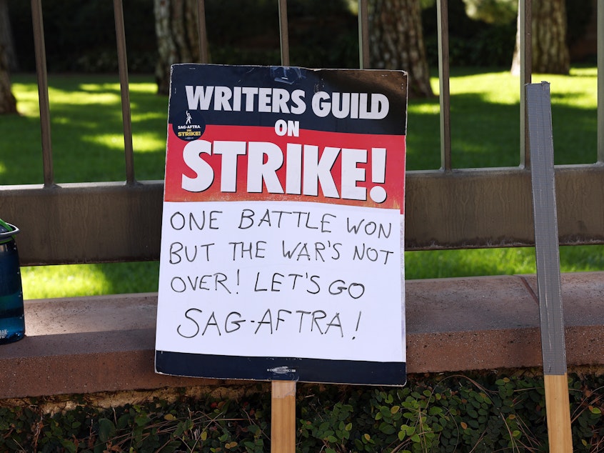 caption: A WGA support sign rests near SAG-AFTRA members picketing outside Warner Bros. Studio as the actors strike continues on September 26, 2023 in Burbank, California.