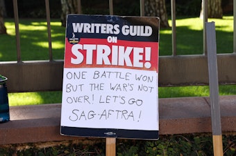 caption: A WGA support sign rests near SAG-AFTRA members picketing outside Warner Bros. Studio as the actors strike continues on September 26, 2023 in Burbank, California.