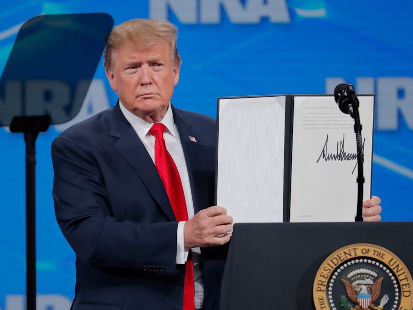 caption: President Trump holds up an executive order he signed at an NRA event Friday, announcing that the United States will drop out of the Arms Trade Treaty that was signed during the Obama administration.