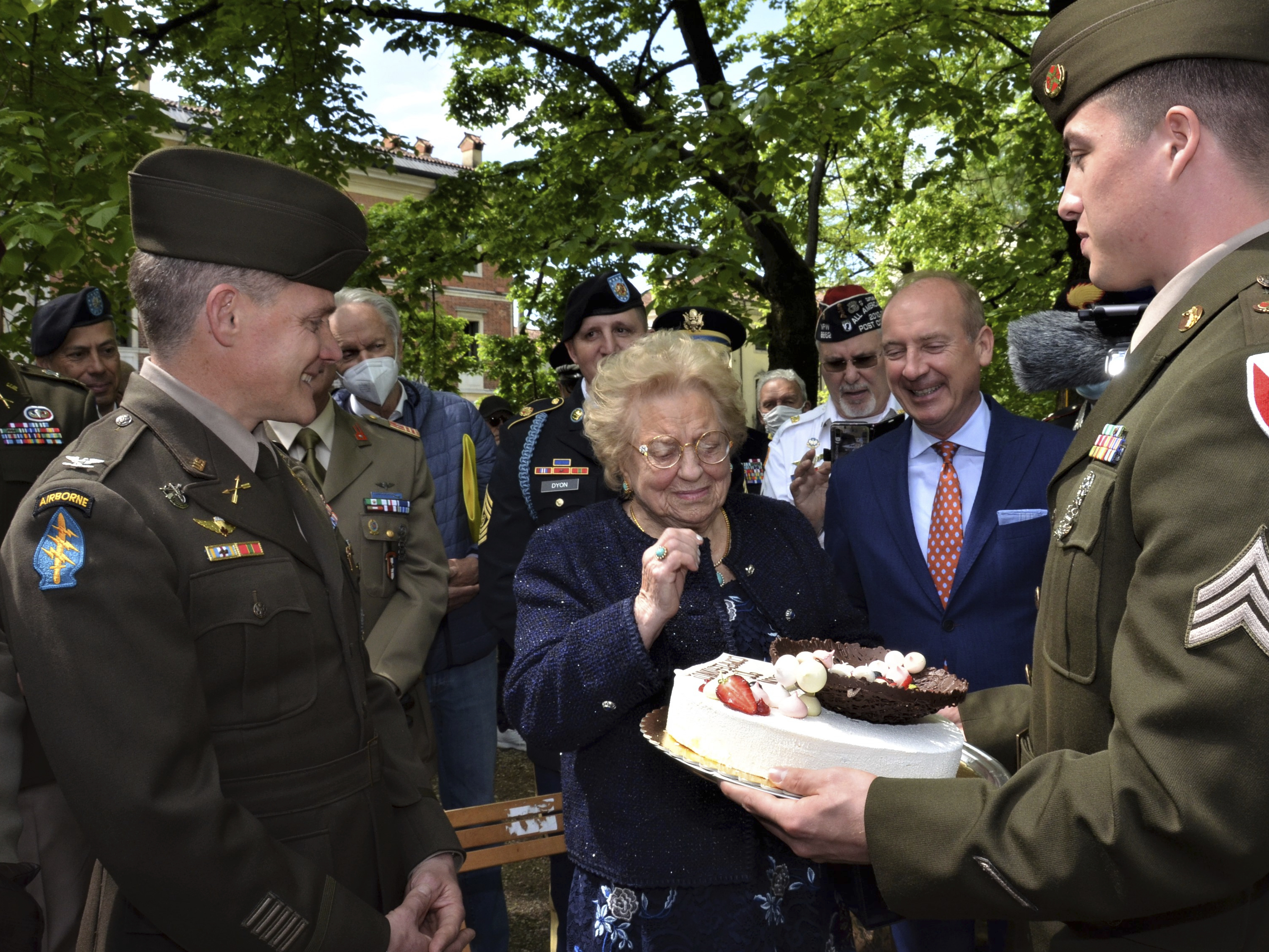 caption: Soldiers from U.S. Army Garrison Italy return a birthday cake to Meri Mion, center, in Vicenza, northern Italy, Thursday, April 28, 2022, to replace the one U.S. soldiers ate as they entered her hometown during one of the final battles of World War II. Mion, who turns 90 on Friday, wiped away tears as she was presented with the cake.