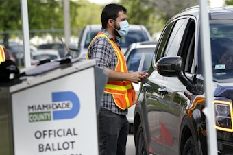 caption: An election worker takes ballots from voters dropping them off at an official ballot drop box at the Miami-Dade County Board of Elections.