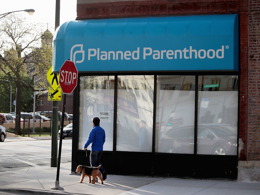 caption: A person walks by a Planned Parenthood clinic on May 18, 2018 in Chicago. Under the new rule, posted Friday by the federal Department of Health and Human Services Office of Population Affairs, any organization that provides or refers patients for abortions is ineligible for Title X funding to cover STD prevention, cancer screenings and contraception.
