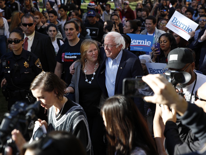caption: Democratic presidential candidate and Vermont Sen. Bernie Sanders and his wife, Jane O'Meara Sanders, lead supporters to an early voting location after a campaign event at the University of Nevada, in Las Vegas on Tuesday.