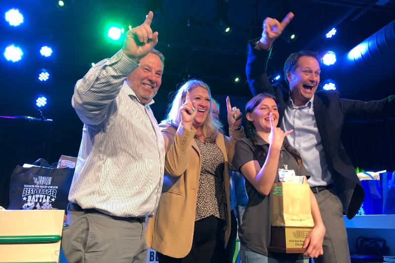 caption: Emma Beeler, holding trophy, is Washington's top bagger of 2023. She poses with contest sponsors, including the Washington Food Industry Association. 