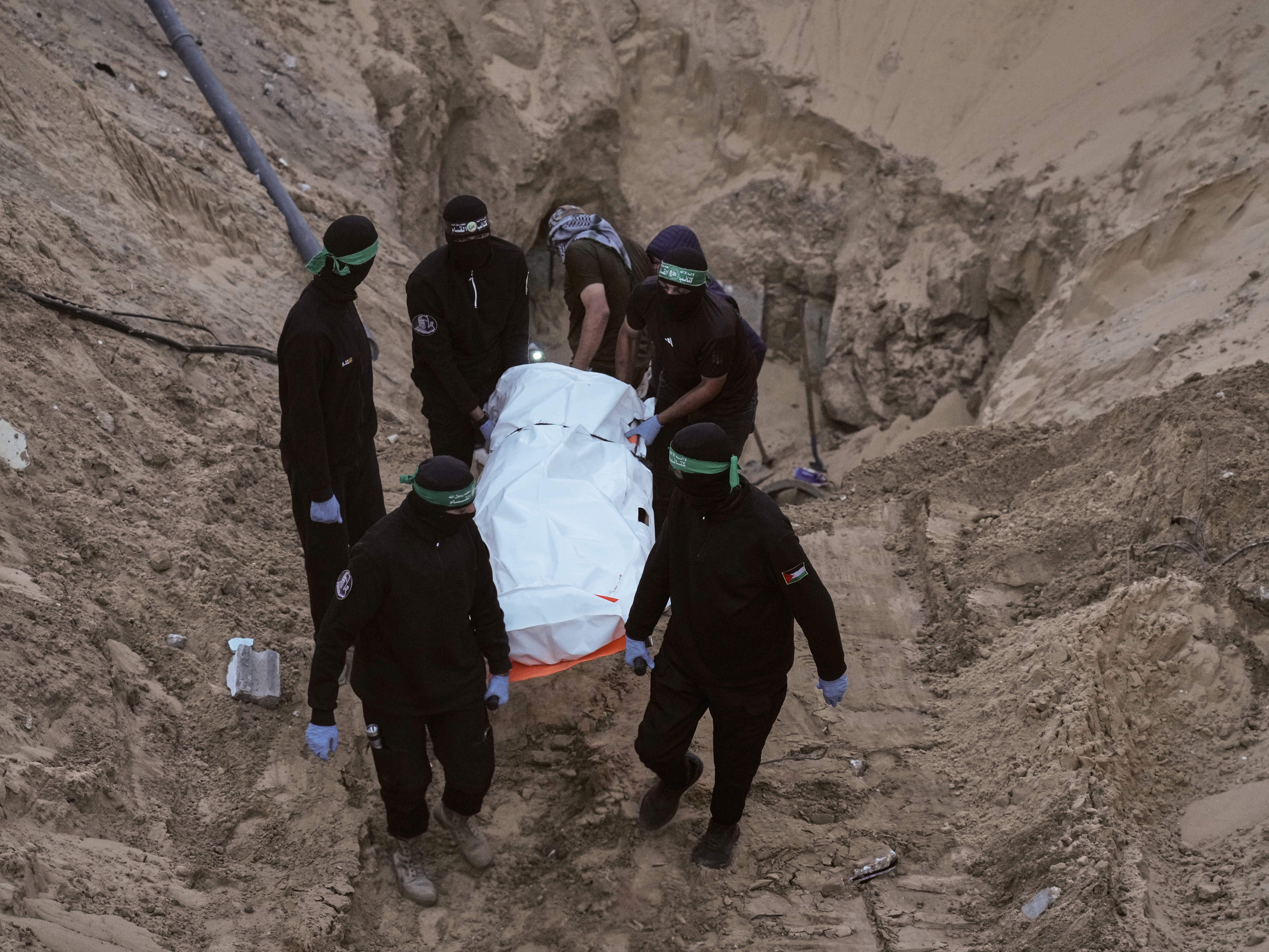 caption: Hamas militants carry a white bag believed to contain a body, after retrieving it from a tunnel during a search for the remains of hostages in Hamad City, Khan Younis, in southern Gaza, Tuesday, Oct. 28, 2025.