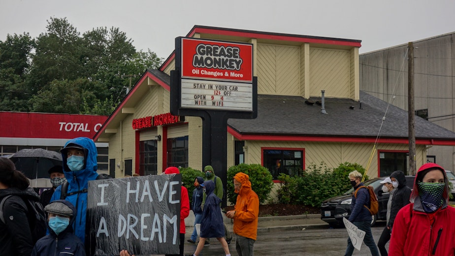 caption: Onlookers stand in front of the Grease Monkey at the intersection of 23rd Avenue and Rainier Avenue as an estimated 60,000 silent marchers pass by on their way from Judkins Park to Jefferson Park on June 12th.