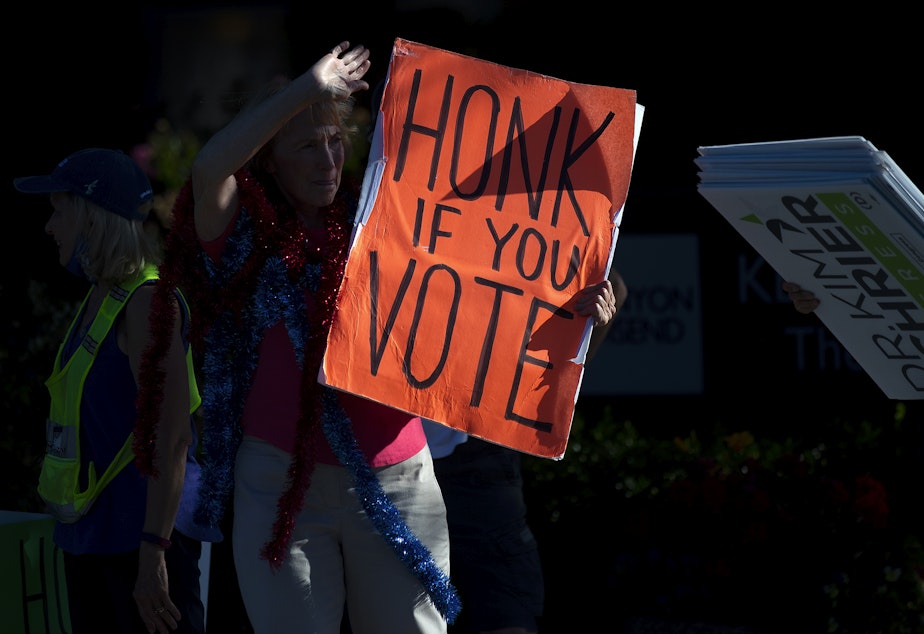 caption: Honk if you vote reads a sign as a crowd gathers at the intersection of Sunset Way and East Front Street on Tuesday, August 2, 2022, in Issaquah. 