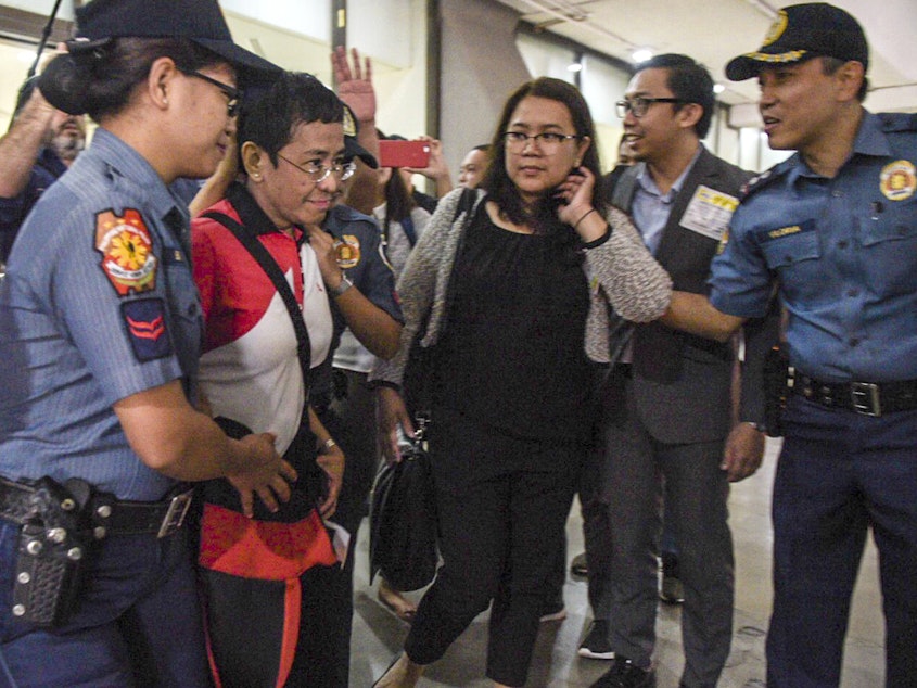caption: In this photo released by Rappler, CEO and Executive Editor Maria Ressa, second from left, is escorted by police after being arrested upon her arrival at Manila's International Airport on Friday.