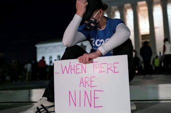 caption: A woman, mourning the death of Ruth Bader Ginsburg, holds a sign at the Supreme Court that reads, "when there are nine," something Ginsburg said to describe when there'd be enough women on the court.