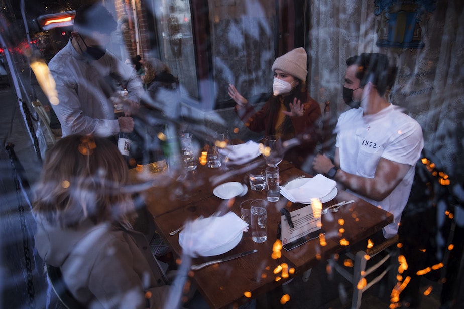 caption: Server Luis Velez opens a bottle of wine for customers Mary Graf, left, Sophie Mandel and Andy Peraza, right, shown through a sheet of plastic surrounding the table, on Wednesday, October 21 , 2020, at Spinasse on Capitol Hill in Seattle.