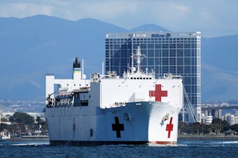 caption: Navy medical and support personnel staff the USNS Mercy, but the hospital ship belongs to the Navy's Military Sealift Command and is run by a crew of civilian mariners. The ship headed to the Port of Los Angeles on March 23 in response to the coronavirus pandemic.