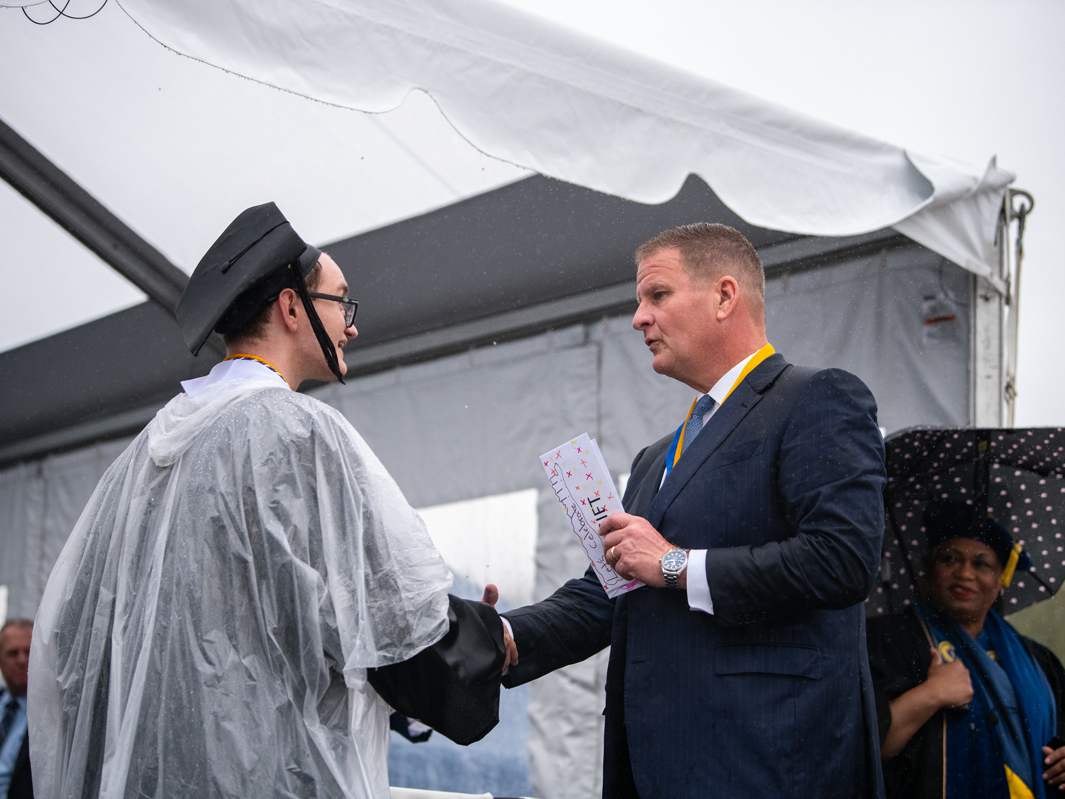 caption: Robert Hale gives an envelope with cash to a graduating UMass Dartmouth student at last week's commencement. Each of the 1,200 graduates received $1,000 onstage, half to keep and half to donate.