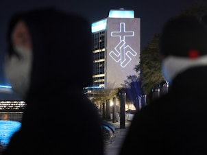 caption: Members of the white nationalist group National Socialist Florida use a laser projector to display white nationalist and anti-LGBTQ images on the side of the CSX building and other high-rise buildings in Jacksonville, Fla.