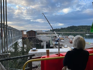 caption: A ferry passenger watches construction on a new walkway that is being built at the Bainbridge Island ferry terminal on Sept. 7, 2023.
