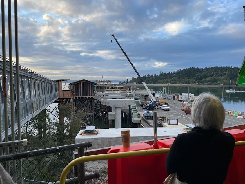 caption: A ferry passenger watches construction on a new walkway that is being built at the Bainbridge Island ferry terminal on Sept. 7, 2023.