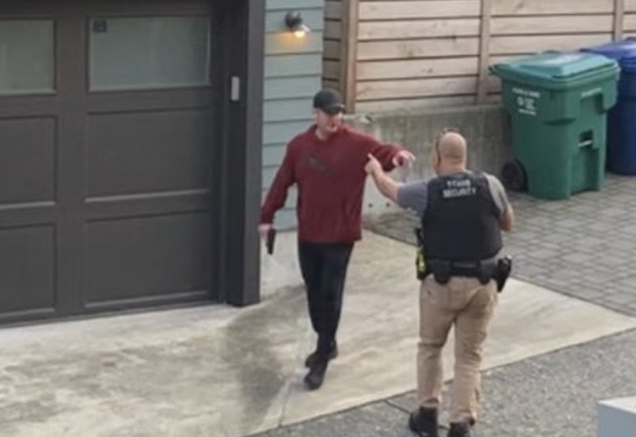 caption: A video still of the suspected shooter, in the crimson hoodie, and Nigel Moss, right, moments before the shooting.