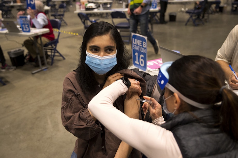 caption: Shiva Sharma, 25, receives a Covid-19 vaccine from volunteer Pharmacist Beth Hykes on Thursday, April 15, 2021, at Lumen Field Event Center in Seattle. As of Thursday, anyone 16 years of age and older is eligible. 