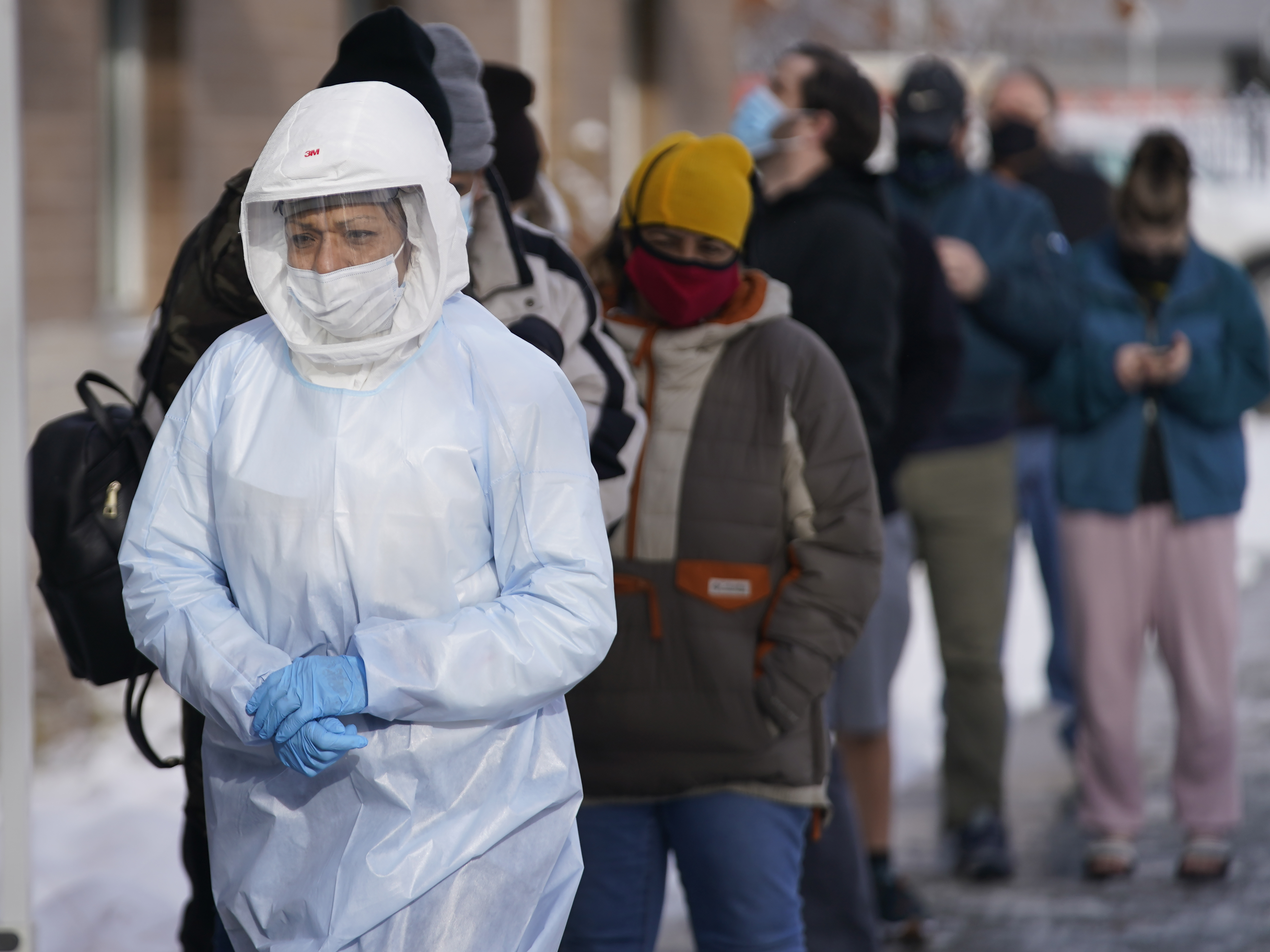 caption: A member of the Salt Lake County Health Department COVID-19 testing staff walks past a line outside the department on Tuesday. The number of new COVID019 cases hit a record this week, topping numbers from January.