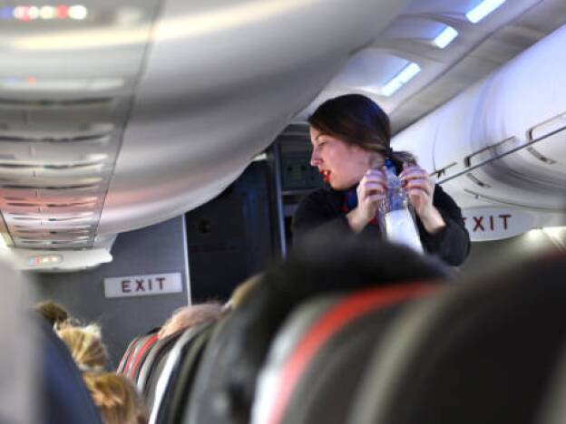 caption: An American Airlines flight attendant serves drinks to passengers after departing Dallas/Fort Worth International Airport.