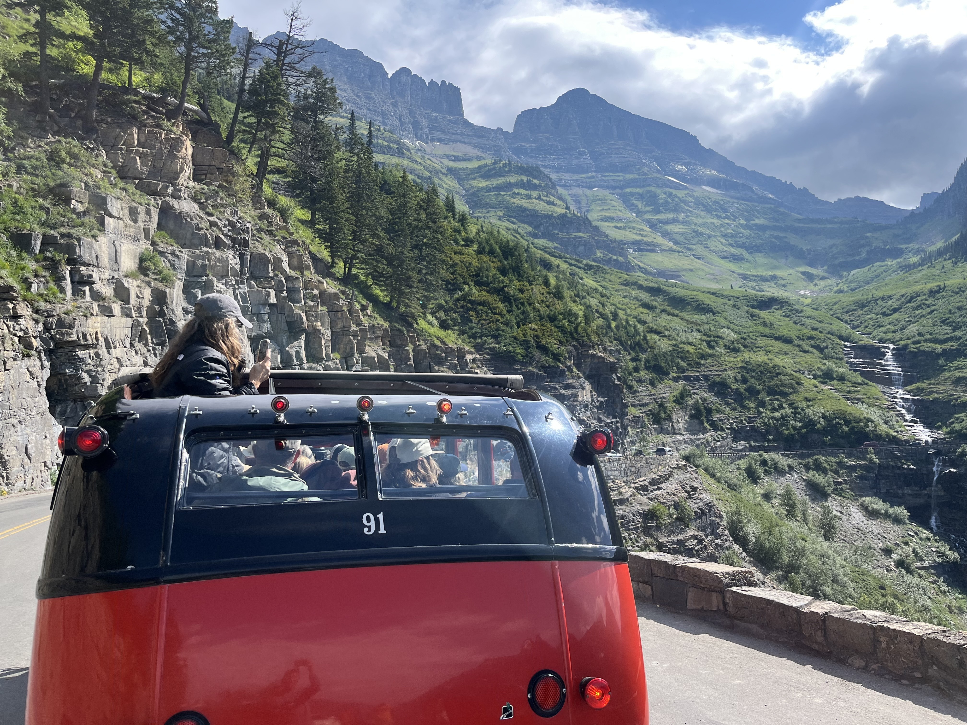 caption: Along Glacier National Park's Going to the Sun Road, tourists admire the view from one of the park's vintage red buses