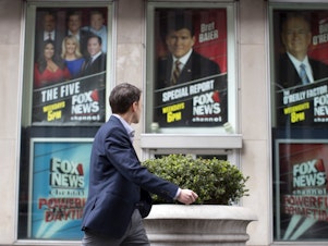 caption: A pedestrian walks past the News Corp. headquarters building in New York displaying posters featuring Fox News Channel personalities on April 19, 2017.