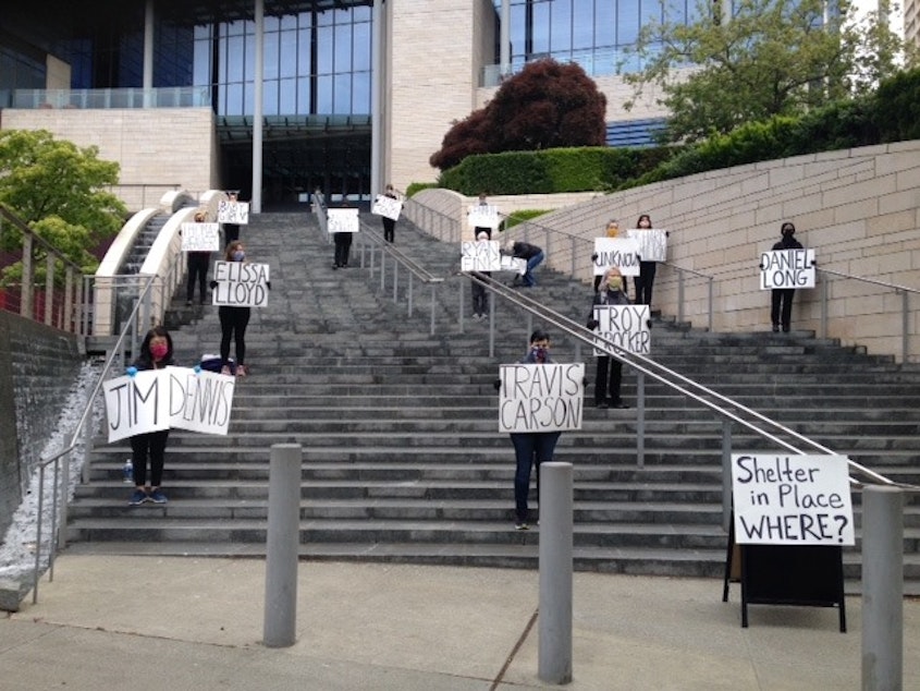 caption: On May 13, 2020, members of Women in Black stood vigil on the steps of Seattle City Hall wearing face masks and holding name cards for the deceased. Their list included three homeless individuals who reportedly died from Covid-19.