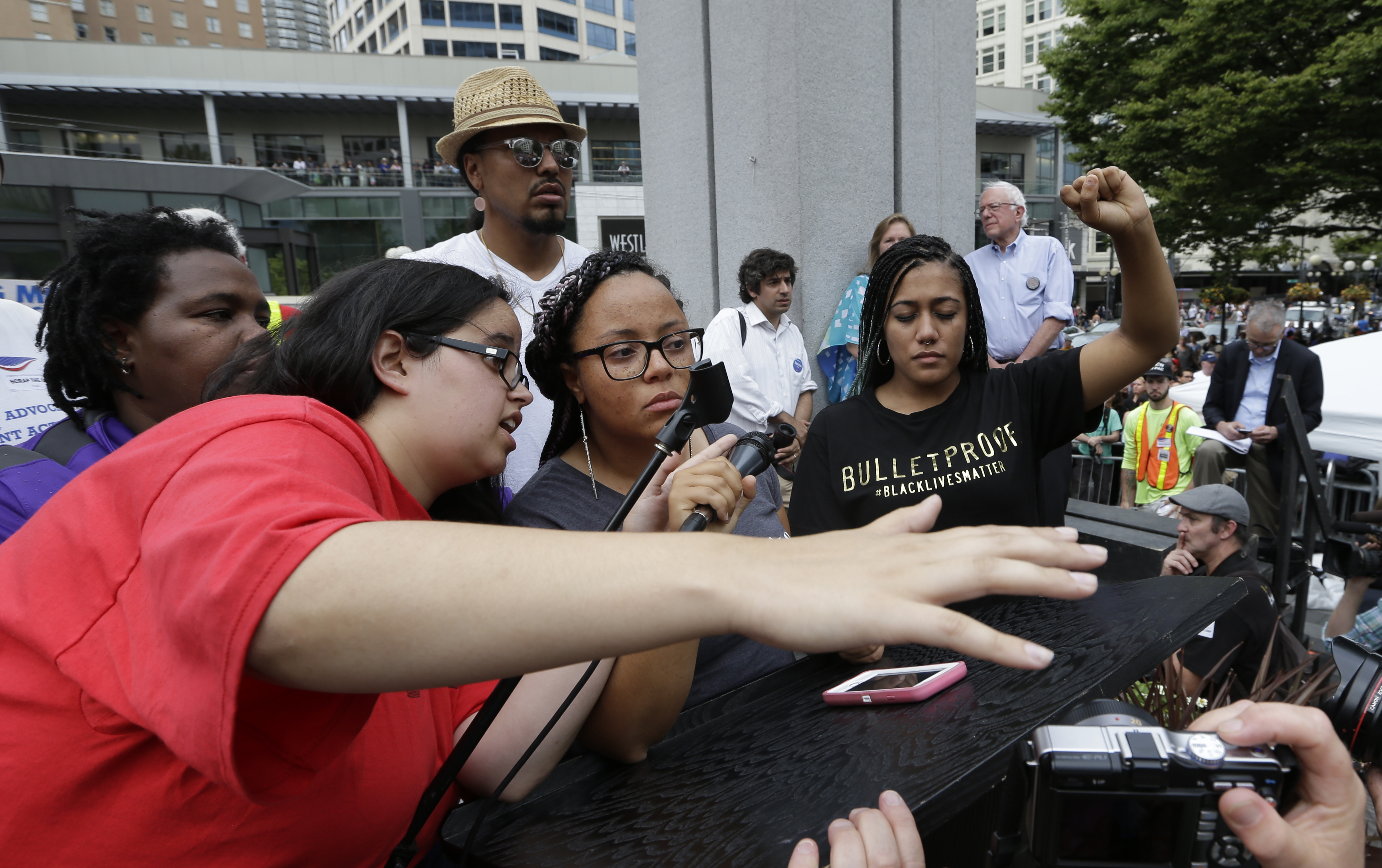 caption: An event organizer, left, tries to persuade two women who had taken over the microphone from Democratic presidential candidate Sen. Bernie Sanders, I-Vt., back right, to relinquish it at a rally Saturday, Aug. 8, 2015.