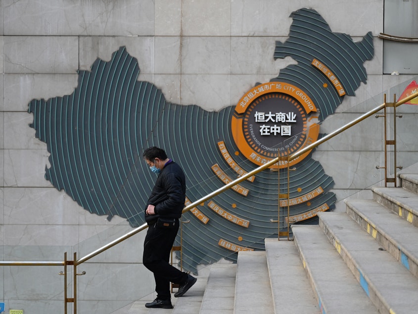 caption: At a partially operating Evergrande commercial complex in Beijing on Monday, a man walks past a map of China that shows Evergrande's commercial complexes throughout the country. Evergrande was once listed as the world's most valuable real estate company, but on Monday, a Hong Kong court ordered it to be liquidated.
