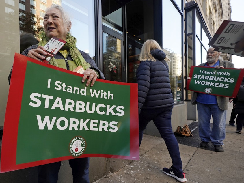 caption: People hold signs supporting Starbucks workers outside a Starbucks on New York's Upper West Side on Thursday.