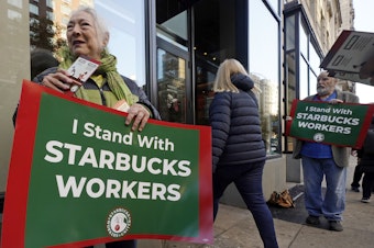 caption: People hold signs supporting Starbucks workers outside a Starbucks on New York's Upper West Side on Thursday.