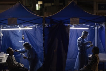 caption: Health workers administer COVID tests outside a building placed under lockdown in Hong Kong on Jan. 6. Hong Kong is imposing strict new COVID measures for the first time in almost a year as the omicron variant seeps into the community.