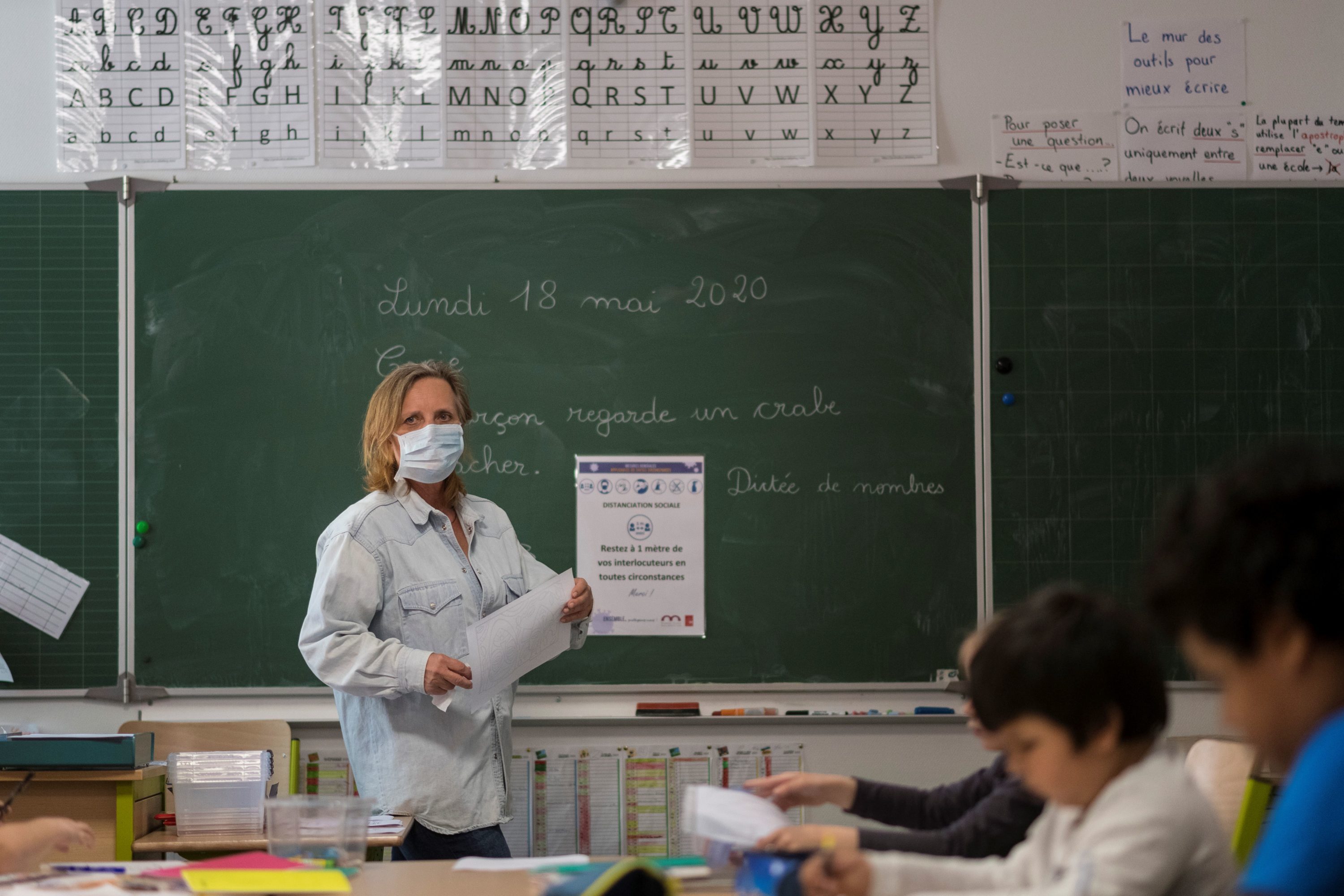 caption: What does school look like in other parts of the world? A teacher gives a lesson at the Cour de Lorraine elementary school in Mulhouse, eastern France, on its re-opening day for pupils, on May 18, 2020. (SEBASTIEN BOZON/AFP via Getty Images)