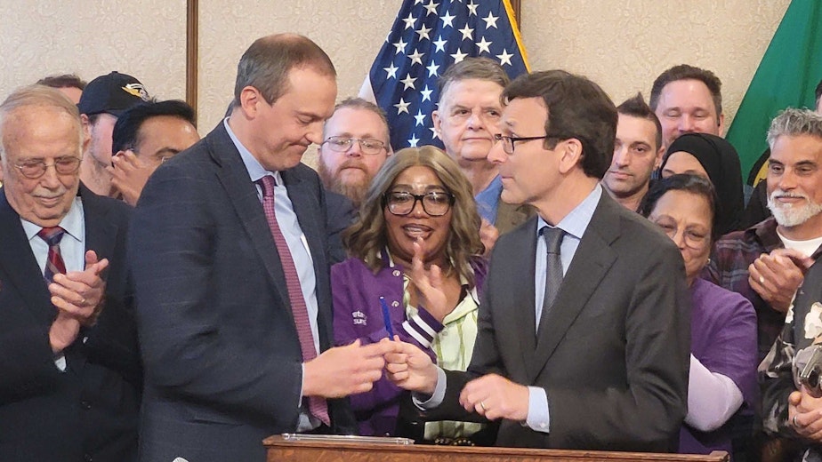 caption: Gov. Bob Ferguson giving an official pen to state Sen. Marcus Riccelli on May 19, 2025.