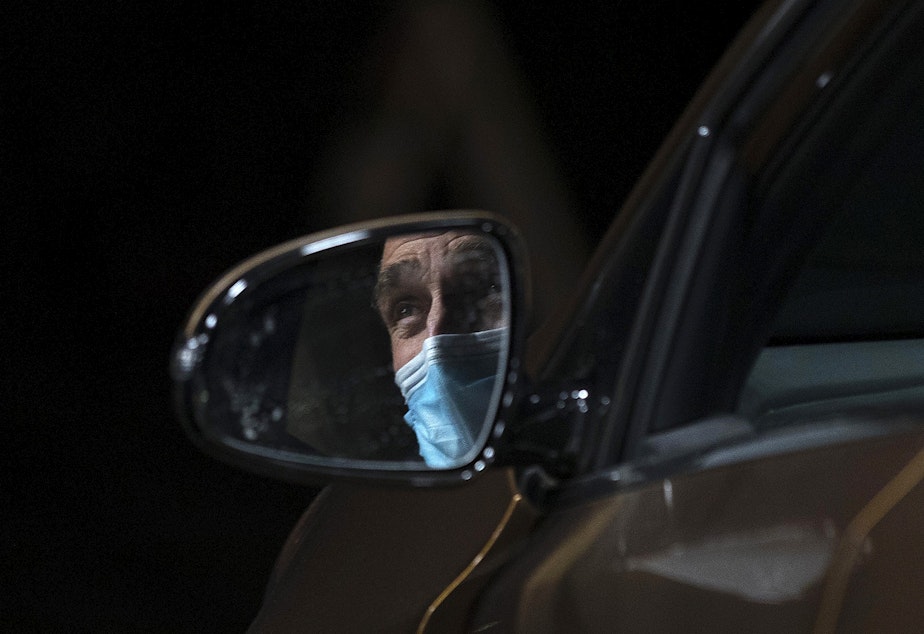 caption: Dennis Haack, a family medicine physician at Neighborcare Health, is shown through a side mirror talking with a healthcare worker while waiting for 15 minutes after receiving his first dose of the Moderna Covid-19 vaccine on Thursday, January 7, 2021, at a drive-thru vaccine clinic for healthcare workers in Renton.