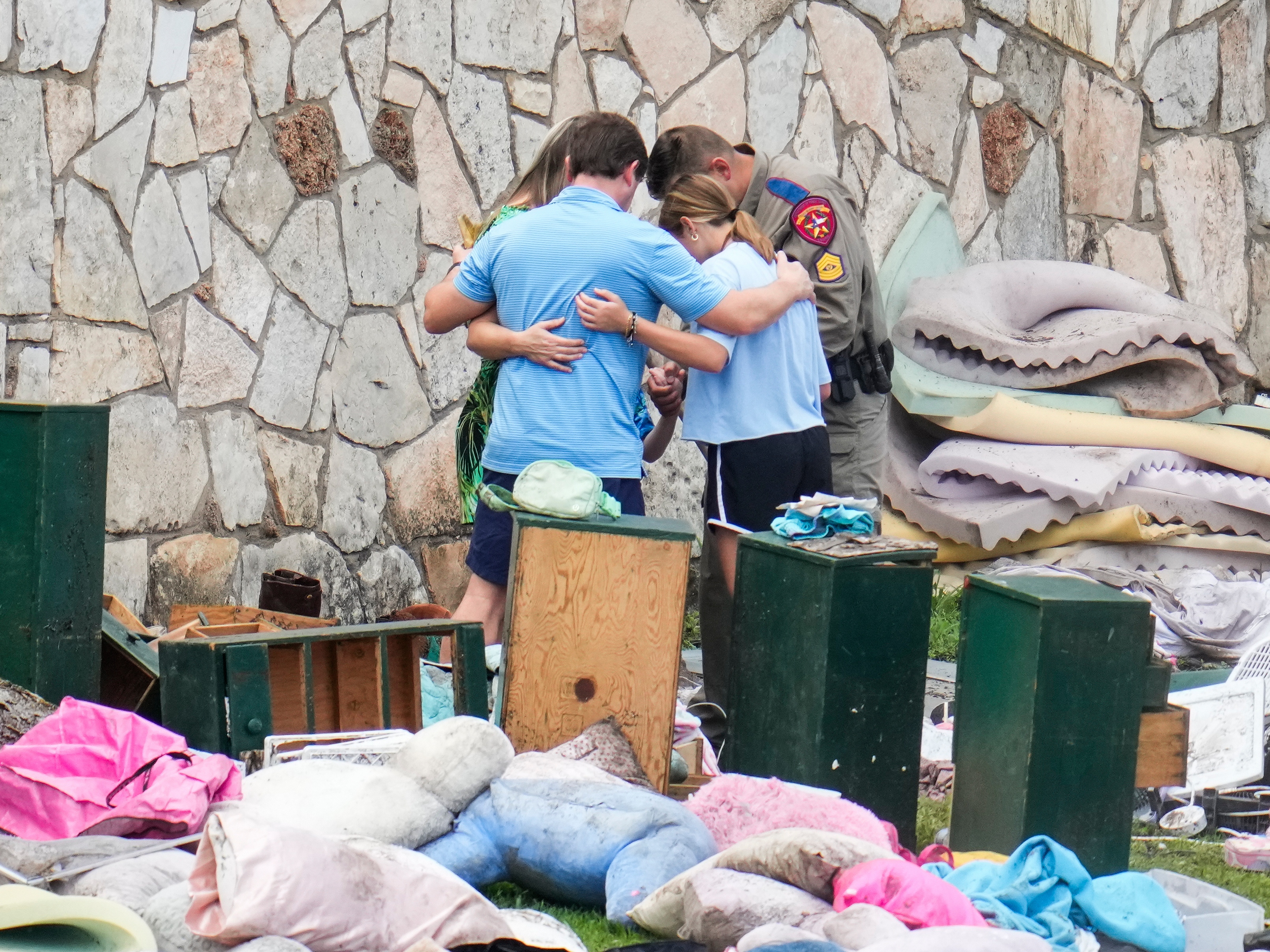 caption: An officer prays with a family as they pick up items at Camp Mystic in Hunt, Texas, on July 9.
