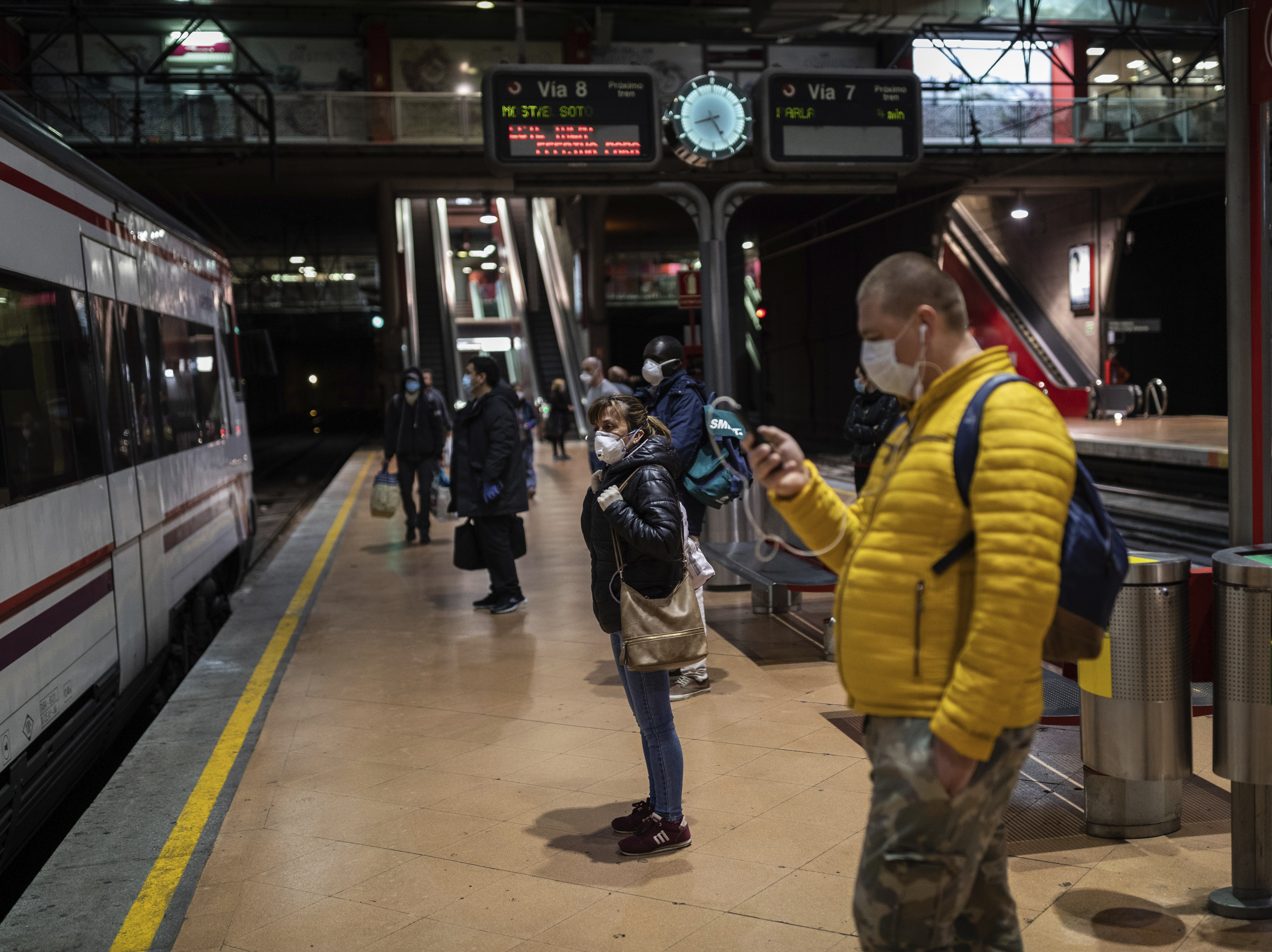 caption: Commuters wearing face masks to protect against coronavirus at the platform of Atocha train station in Madrid, Spain, on Monday. Spain has begun easing restrictions as the number of new cases declines.