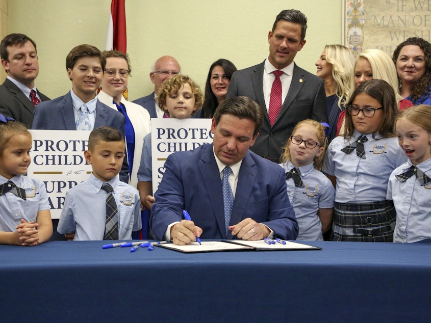 caption: Florida Gov. Ron DeSantis signs the Parental Rights in Education bill, also known as the "Don't Say Gay" bill, at Classical Preparatory School, March 28, 2022, in Shady Hills, Fla. Students and teachers will be able to speak freely about sexual orientation and gender identity in Florida classrooms, provided it's not part of instruction, under a settlement reached Monday, March 11, 2024.
