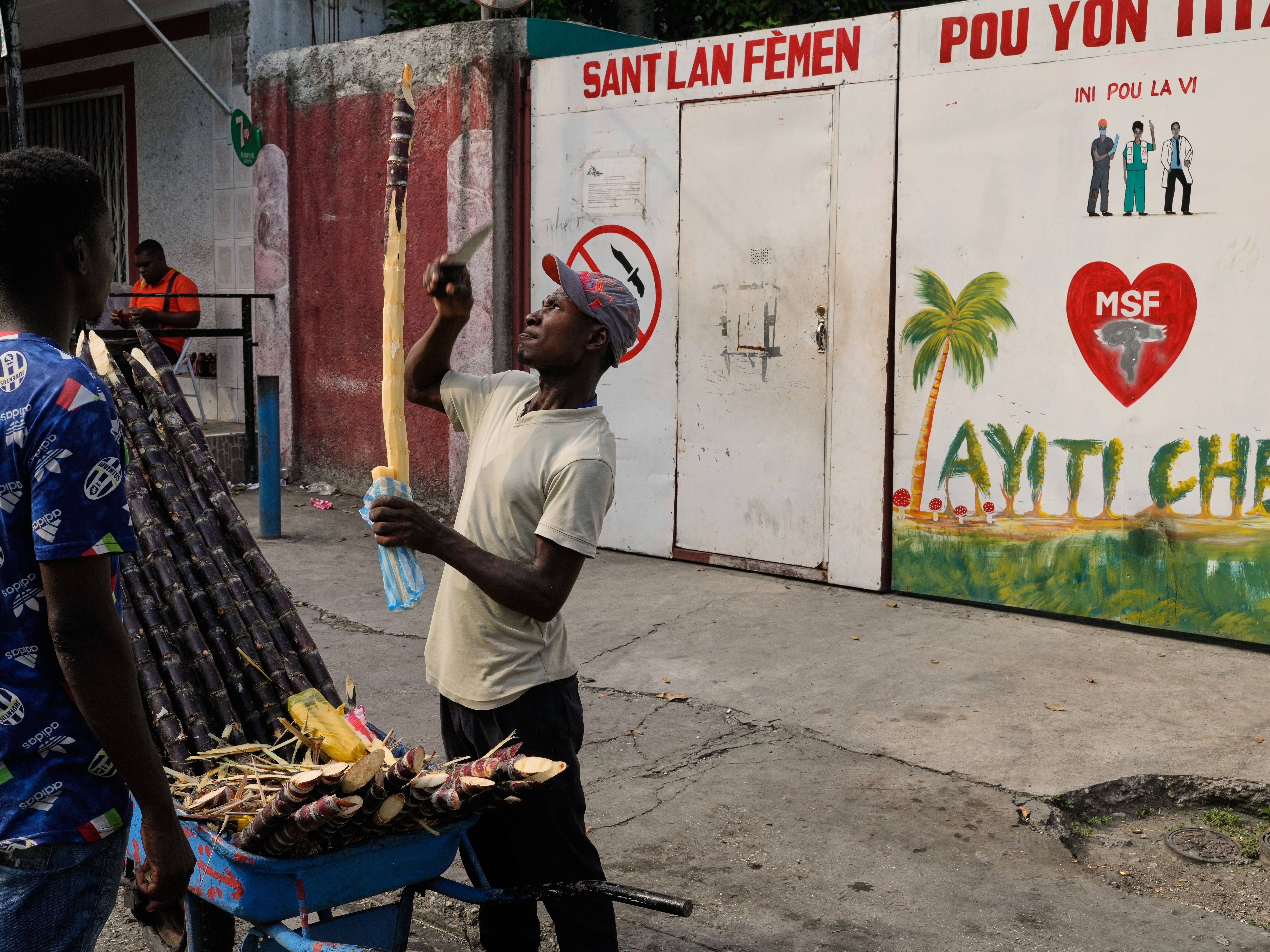 caption: A vendor sells sugarcane next to the entrance of the Doctors Without Borders (MSF) clinic in Port-au-Prince, Haiti, Wednesday, Oct. 15, 2025, after the organization announced the facility's closure due to ongoing violence.