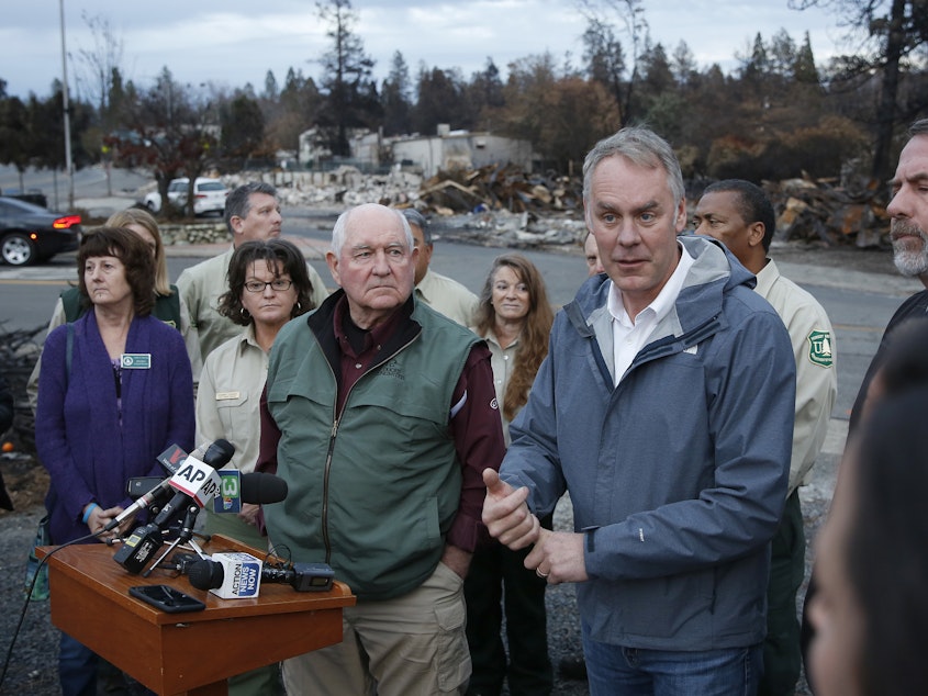 caption: Interior Secretary Ryan Zinke, right, answers a reporters question after touring fire ravaged Paradise, Calif. with Agriculture Secretary Sonny Perdue, center. The pair advocated more aggressive forest management policies to mitigate damage from future wildfires.