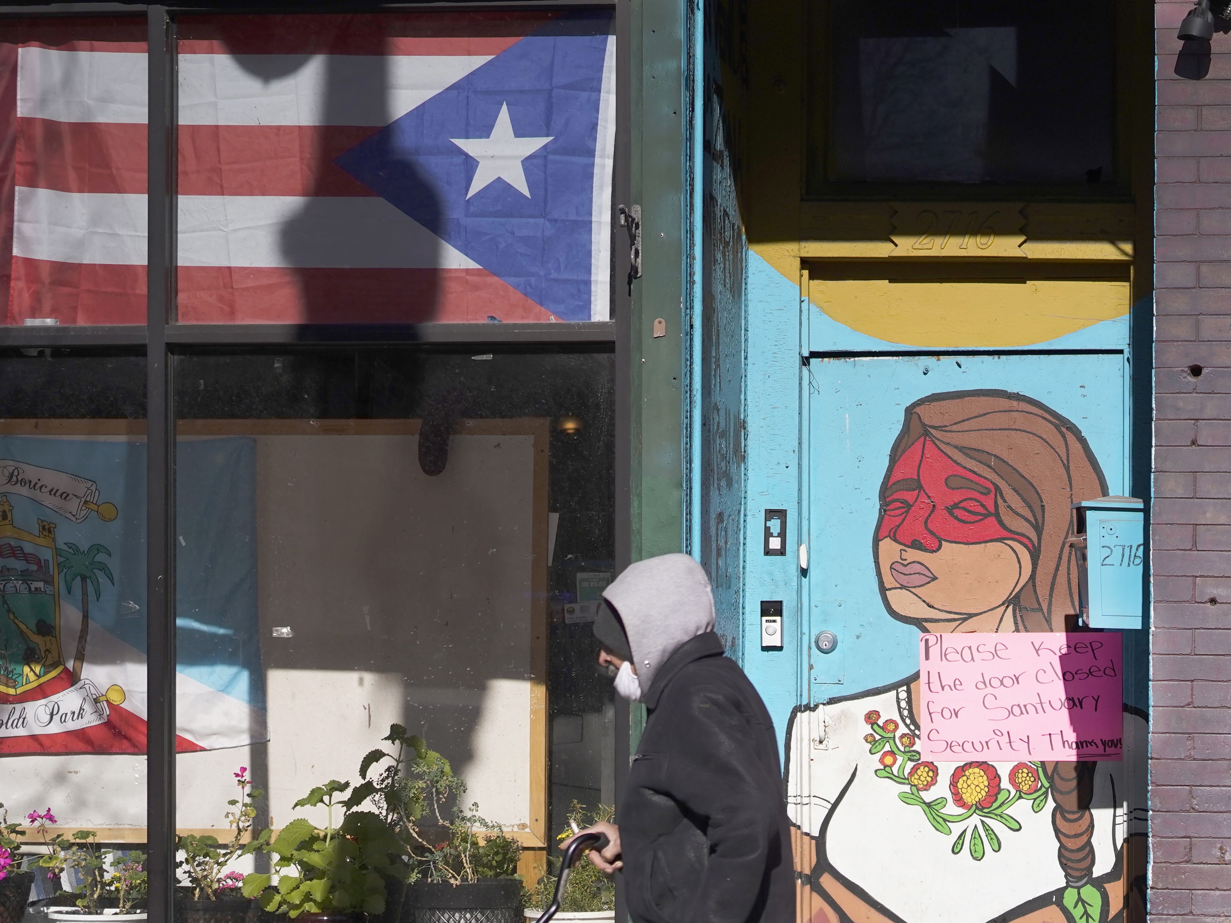 caption: A pedestrian walks past the flag of Puerto Rico and the colorful door to the sanctuary apartment of Chicago's Adalberto Memorial United Methodist Church in Chicago in 2021. The church has provided shelter to immigrants in the U.S. illegally.