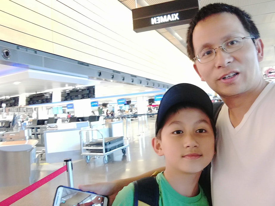 caption: Weibin Zhou (right) poses with his child Phillip Zhou at SeaTac Airport in the late 2010s.