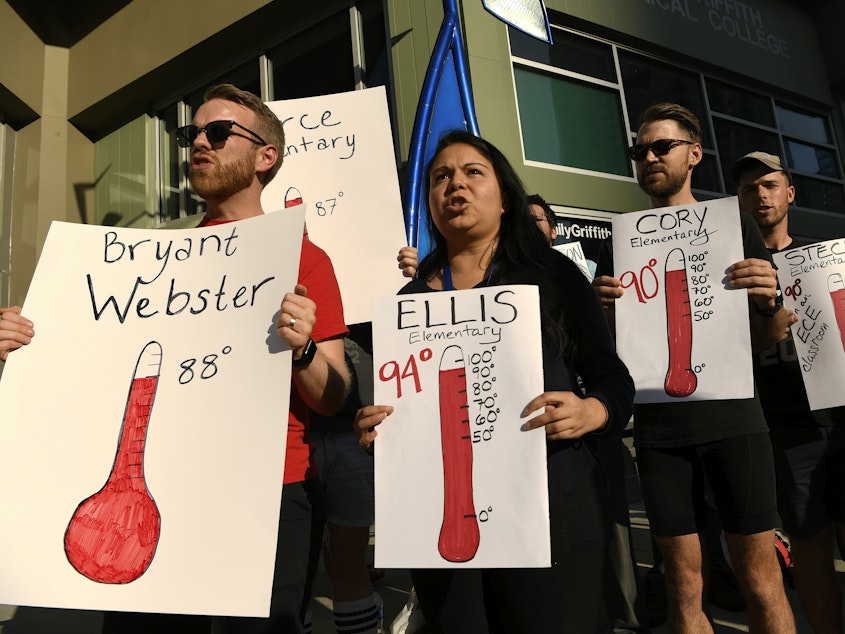 caption: Protesters hold up signs outside of the Denver Public Schools administration building to demand equity for students attending classes in excessively hot classrooms.