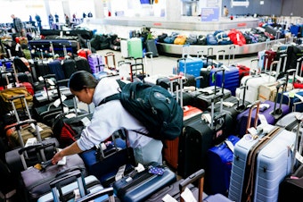 caption: Pristine Floyde searches for a friend's suitcase in a baggage holding area for Southwest Airlines at Denver International Airport in December 2022.